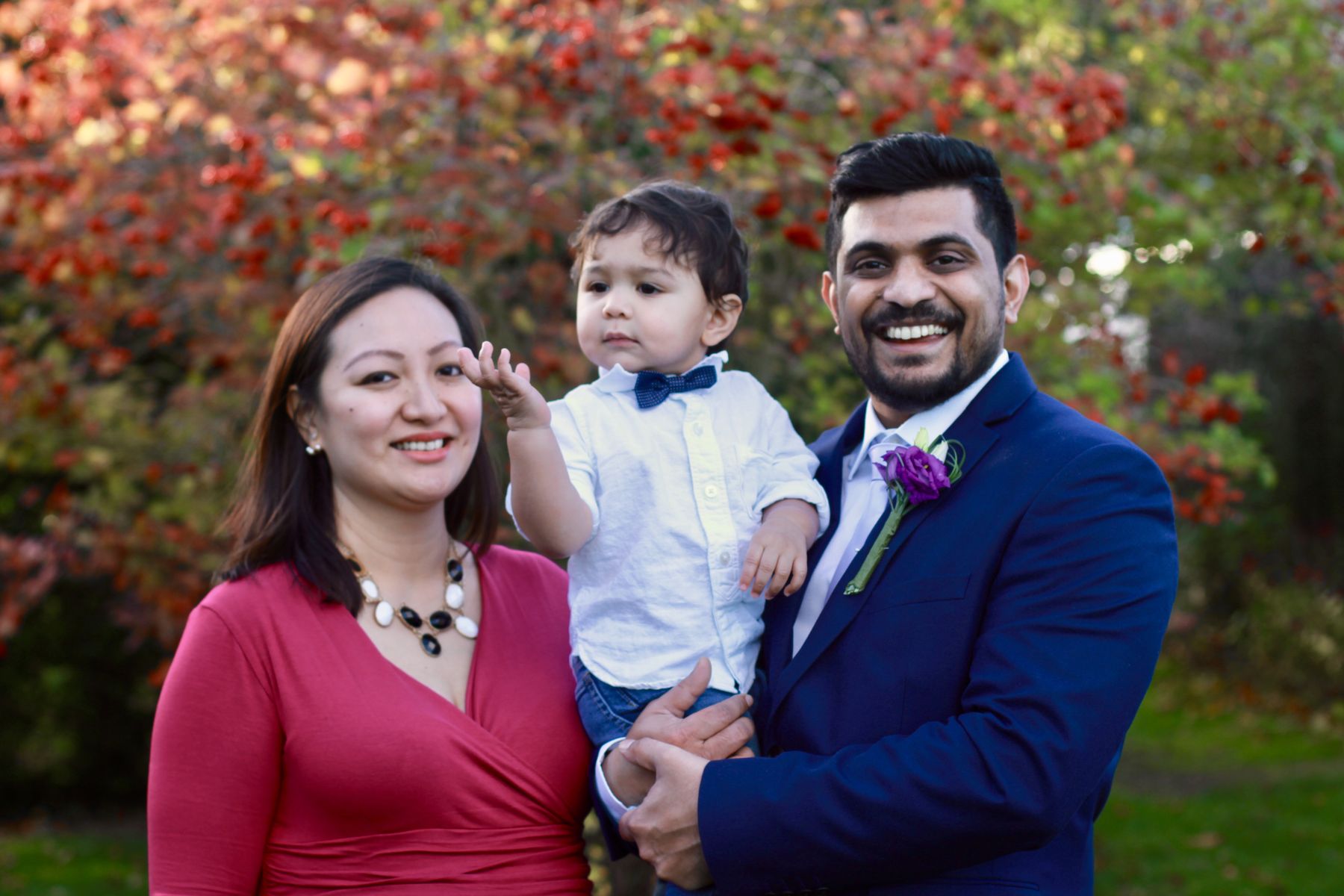 Parents holding their baby son in front of autumn leaves